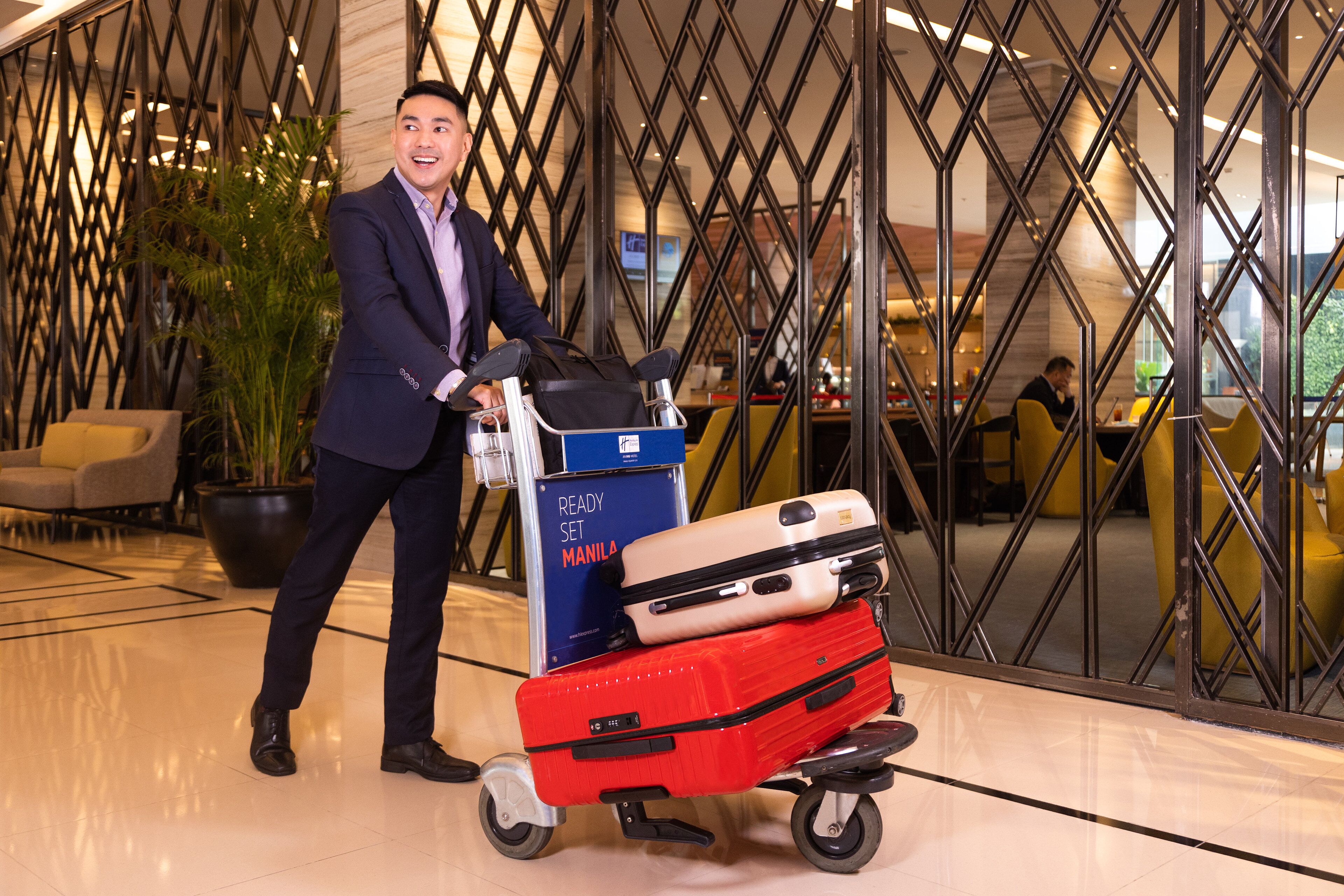 A man pushing a luggage cart with suitcases in a modern lobby with geometric wall design and seating areas.