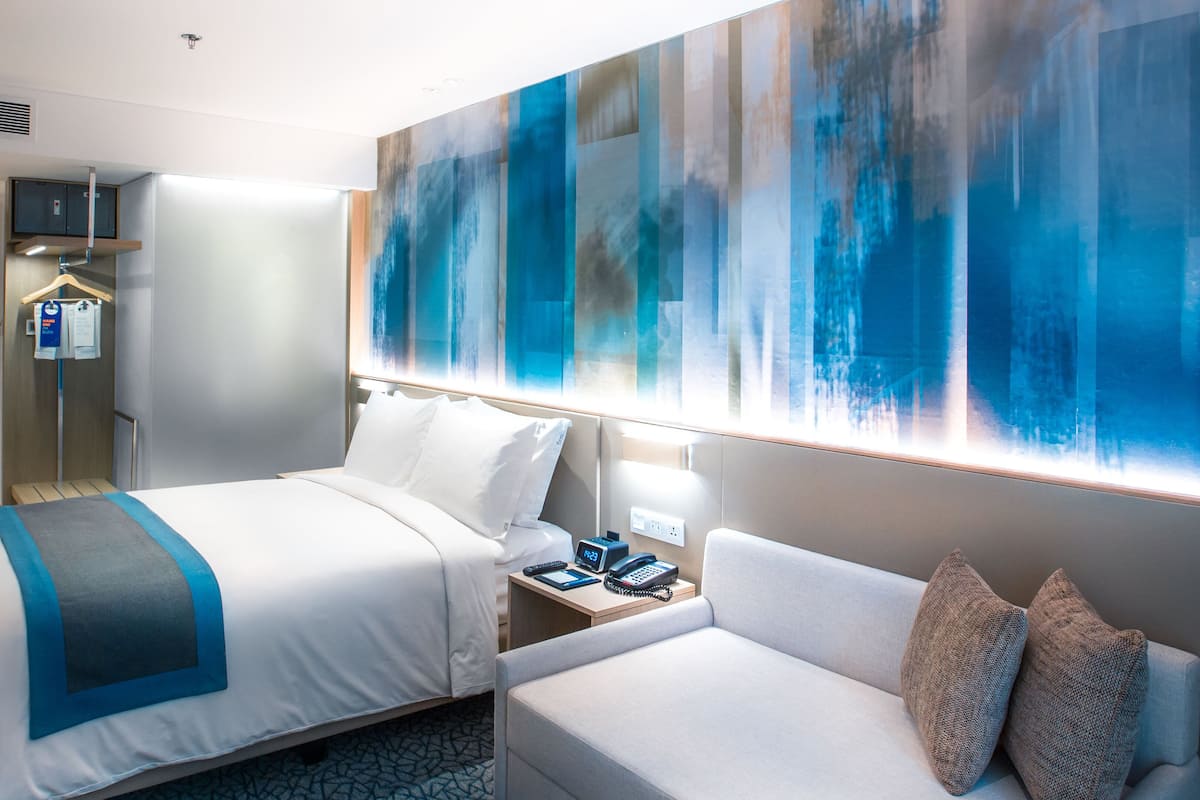 Habitación de hotel con cama, sofá, un cuadro abstracto grande, televisor y armario.