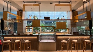 A modern bar area with a glass display case, wooden stools, and a view of greenery through large windows. - Holiday Inn Express Manila Newport City by IHG (Pasay)