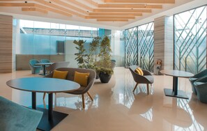 A modern lobby with a large potted plant, seating areas, and a glass wall with a geometric pattern.