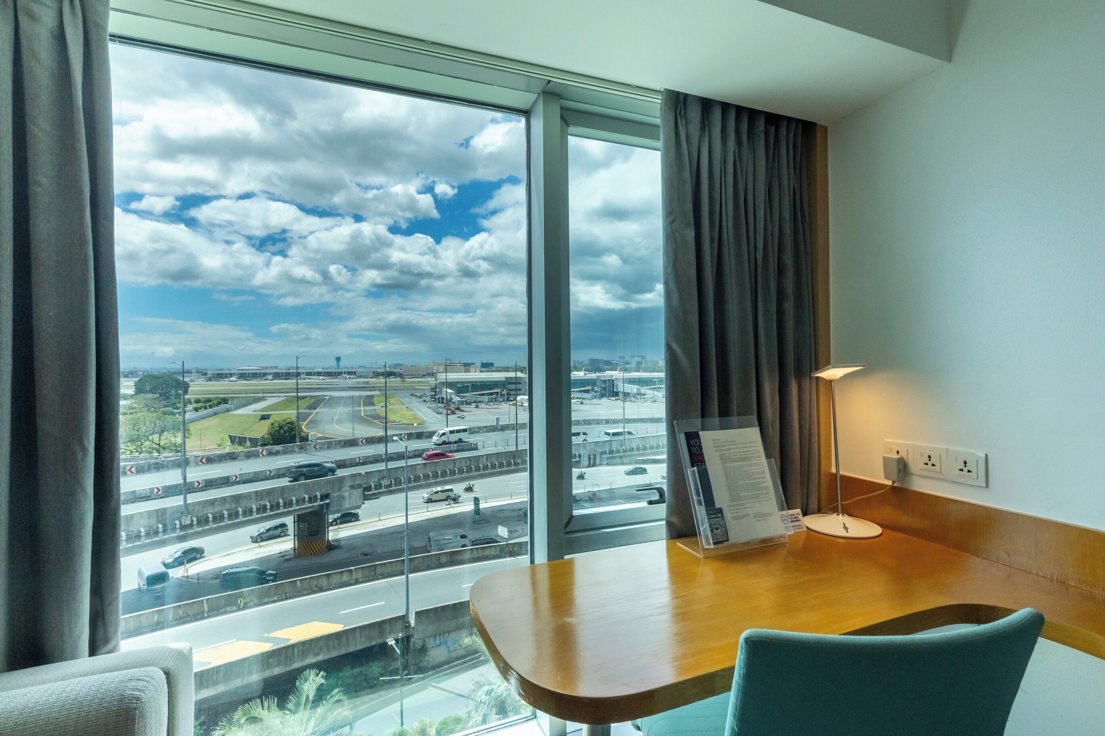 A hotel room with a large window offering a view of a highway and cityscape.