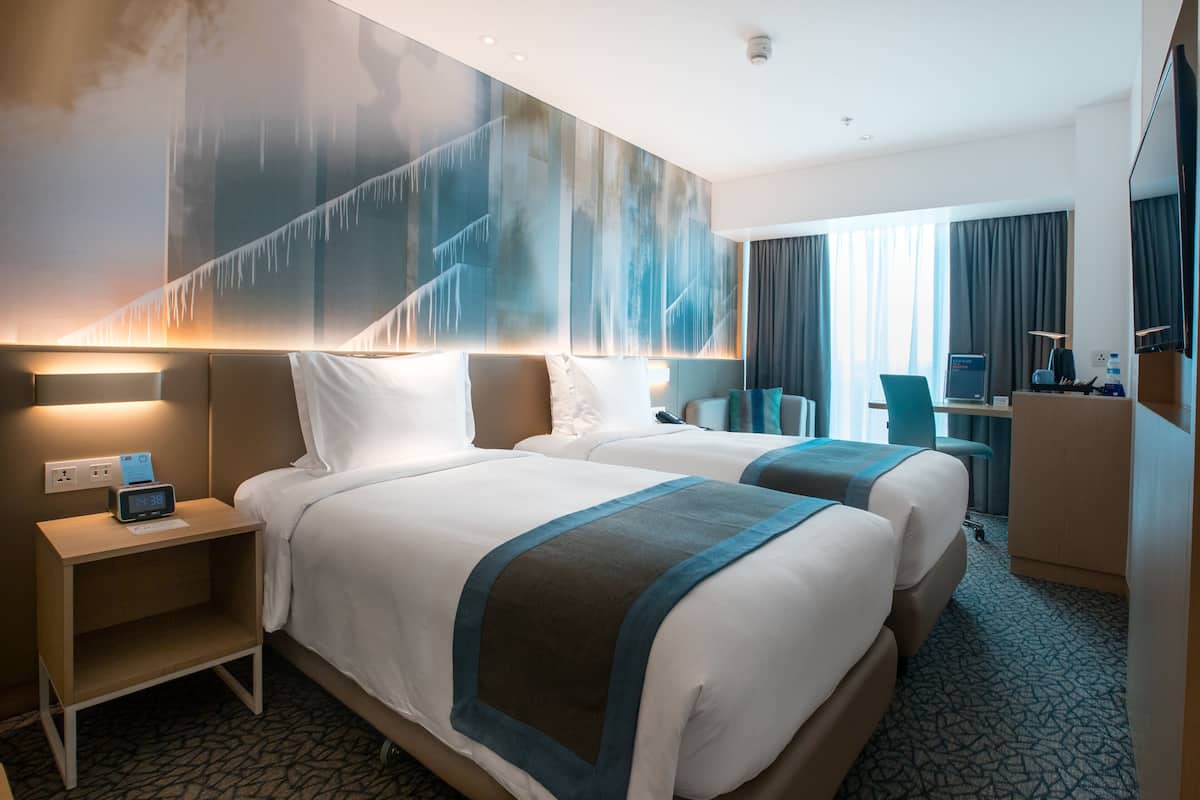 Habitación de hotel con dos camas, un escritorio, una silla y un mural grande en la pared.