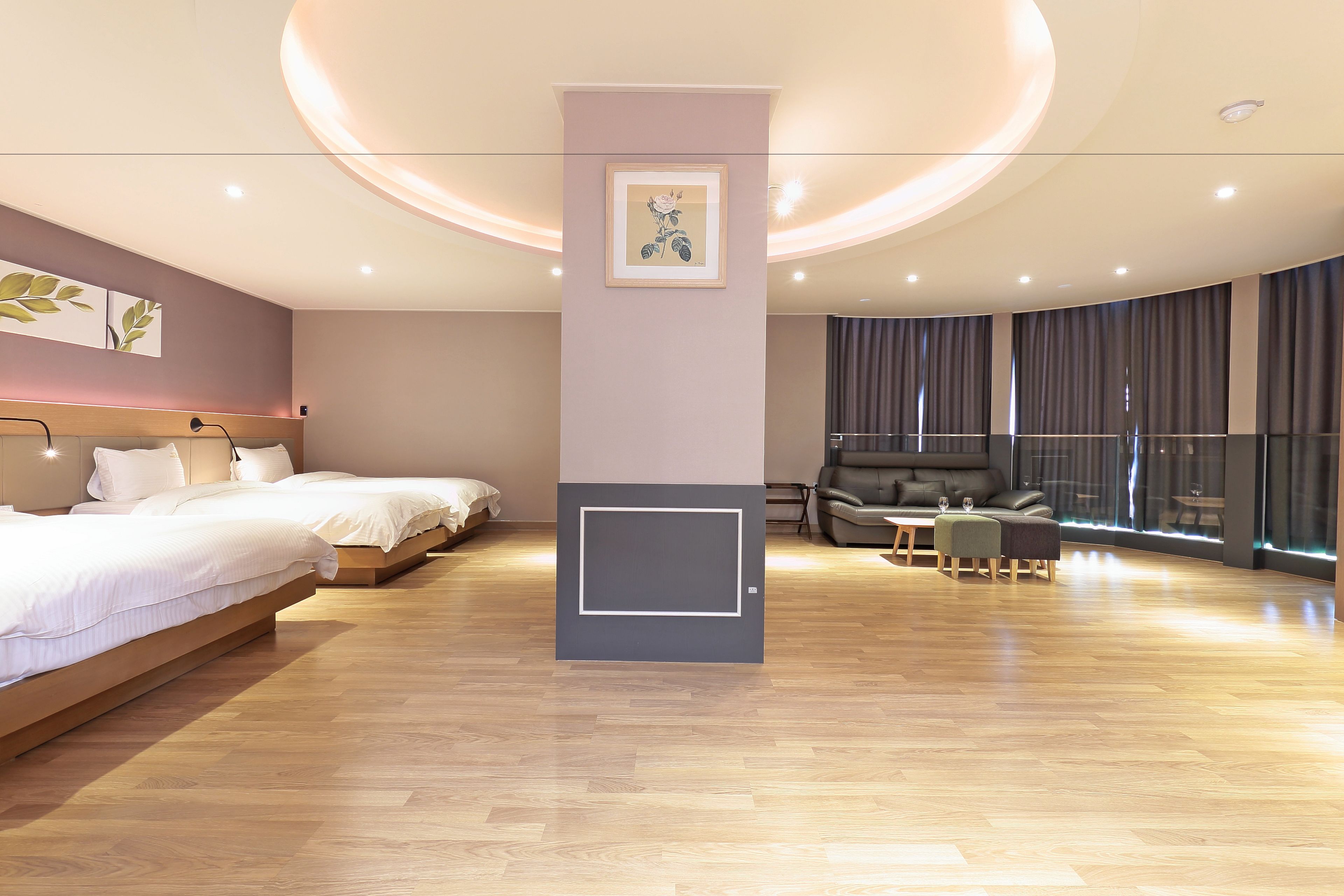 A modern hotel room with two beds, a seating area with a sofa and chairs, and a large window with curtains.