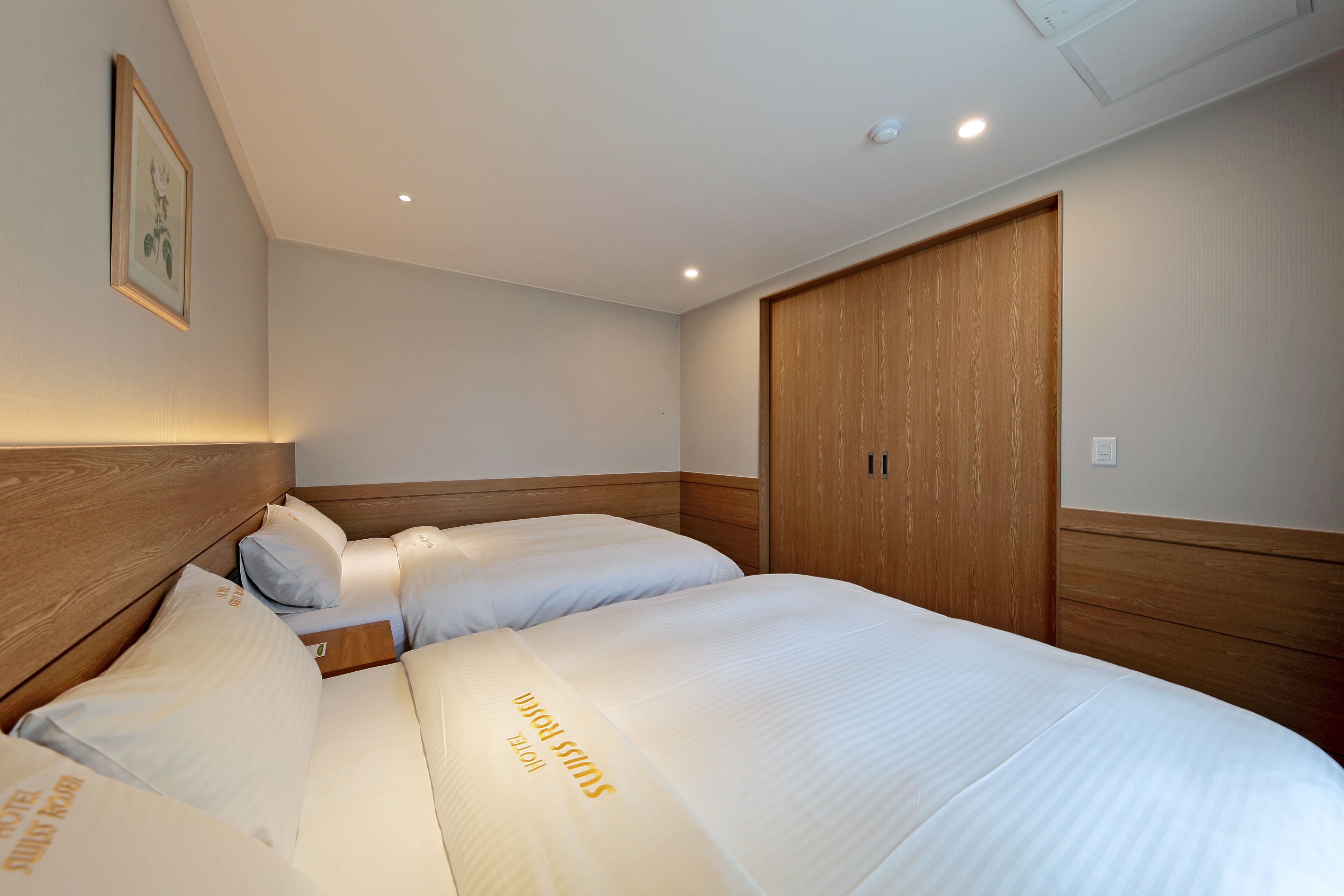 A hotel room with two beds, wooden headboards, a framed picture on the wall, and a wooden wardrobe.