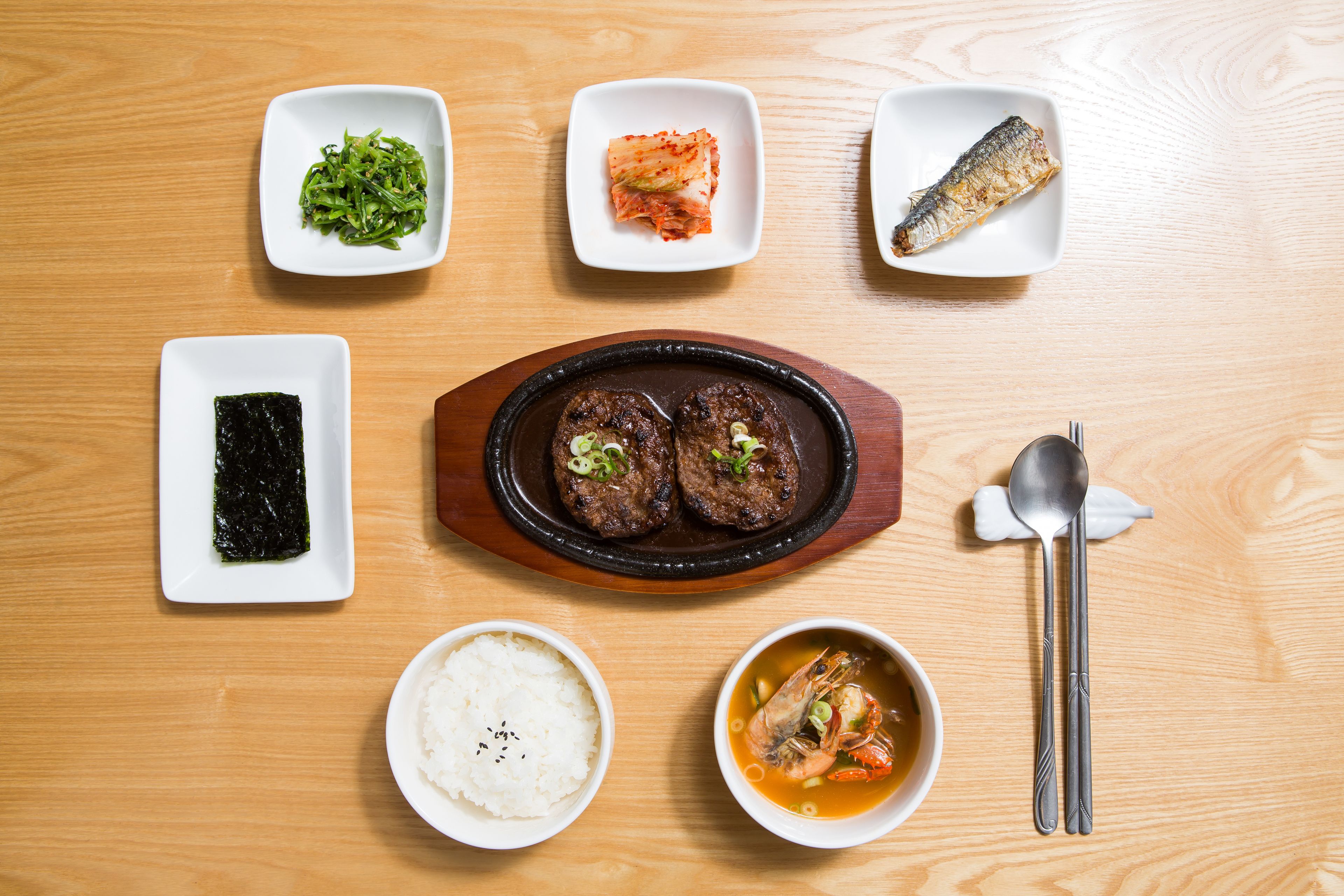 A wooden table with various dishes including rice, soup, and seafood.