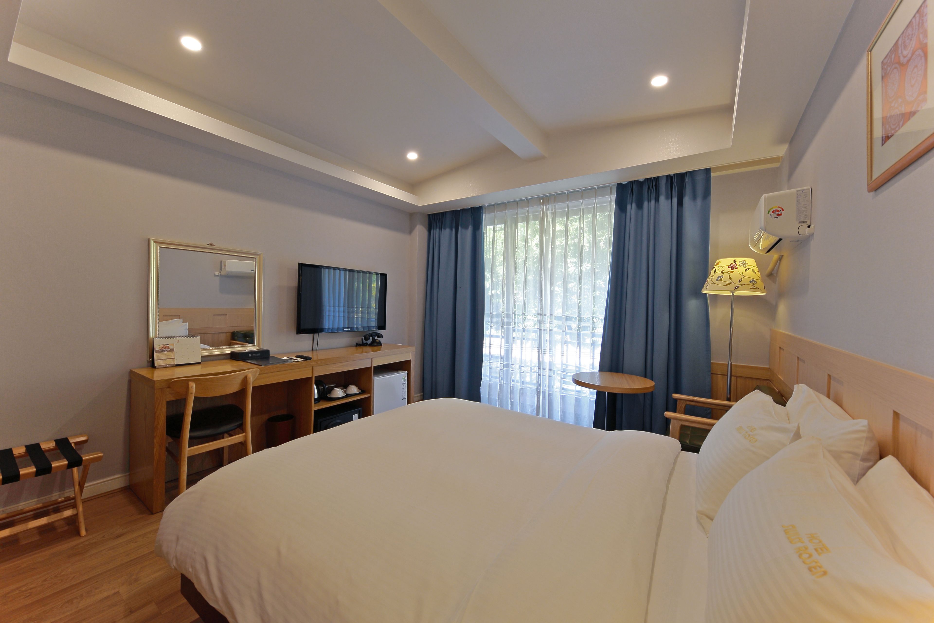 A hotel room with a large bed, a desk with a computer, a television, and a window with curtains.