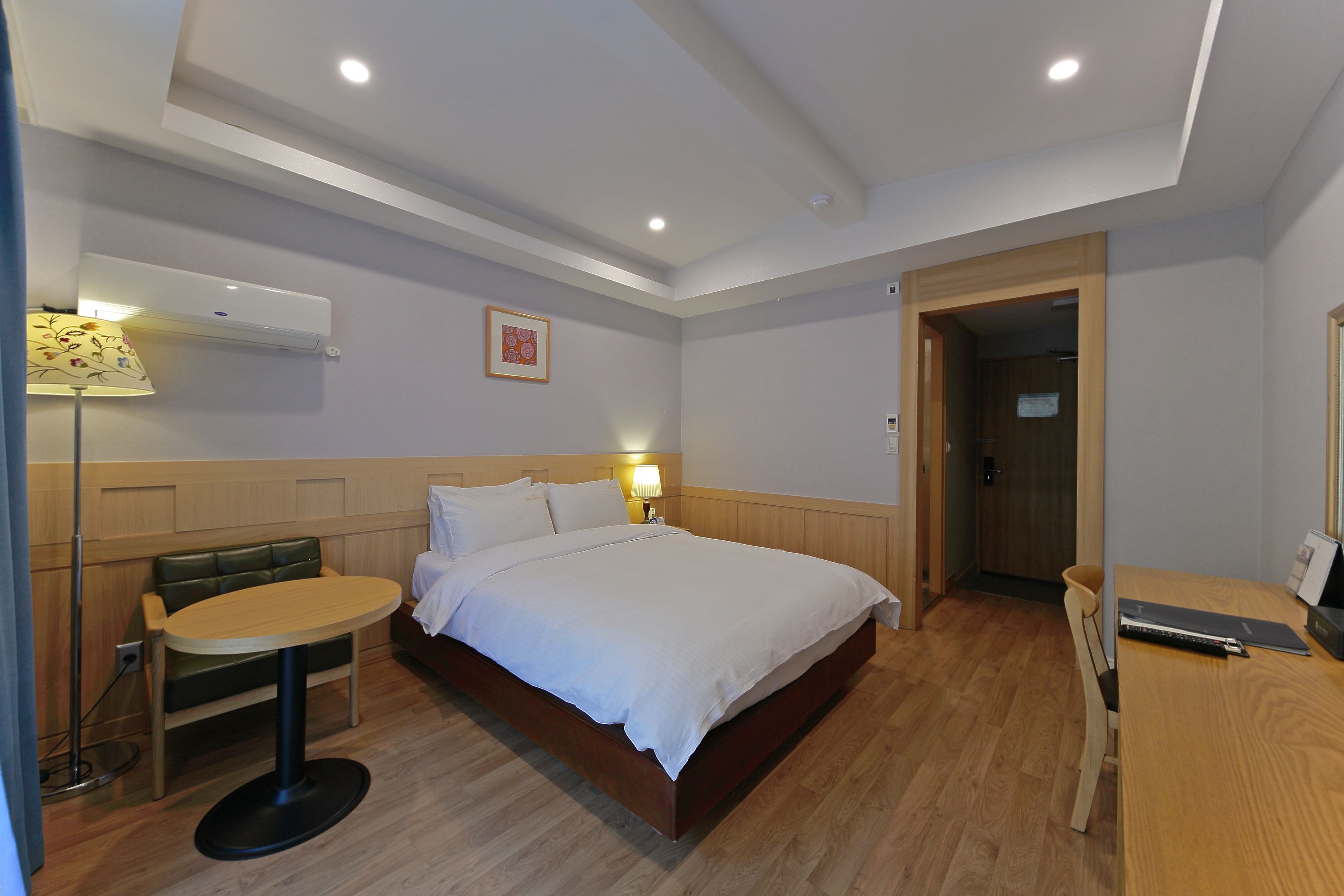 A hotel room with a bed, bedside table, lamp, chair, and a desk with a laptop.