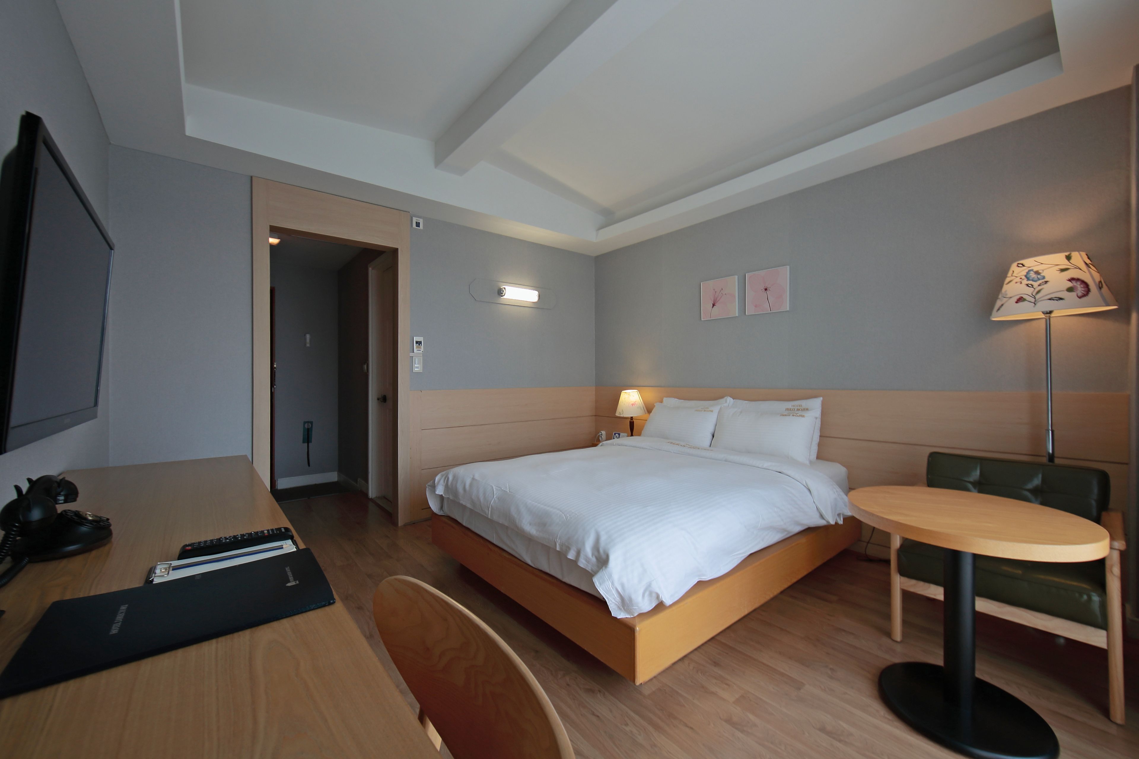 A hotel room with a bed, desk, chair, lamp, and a small table.