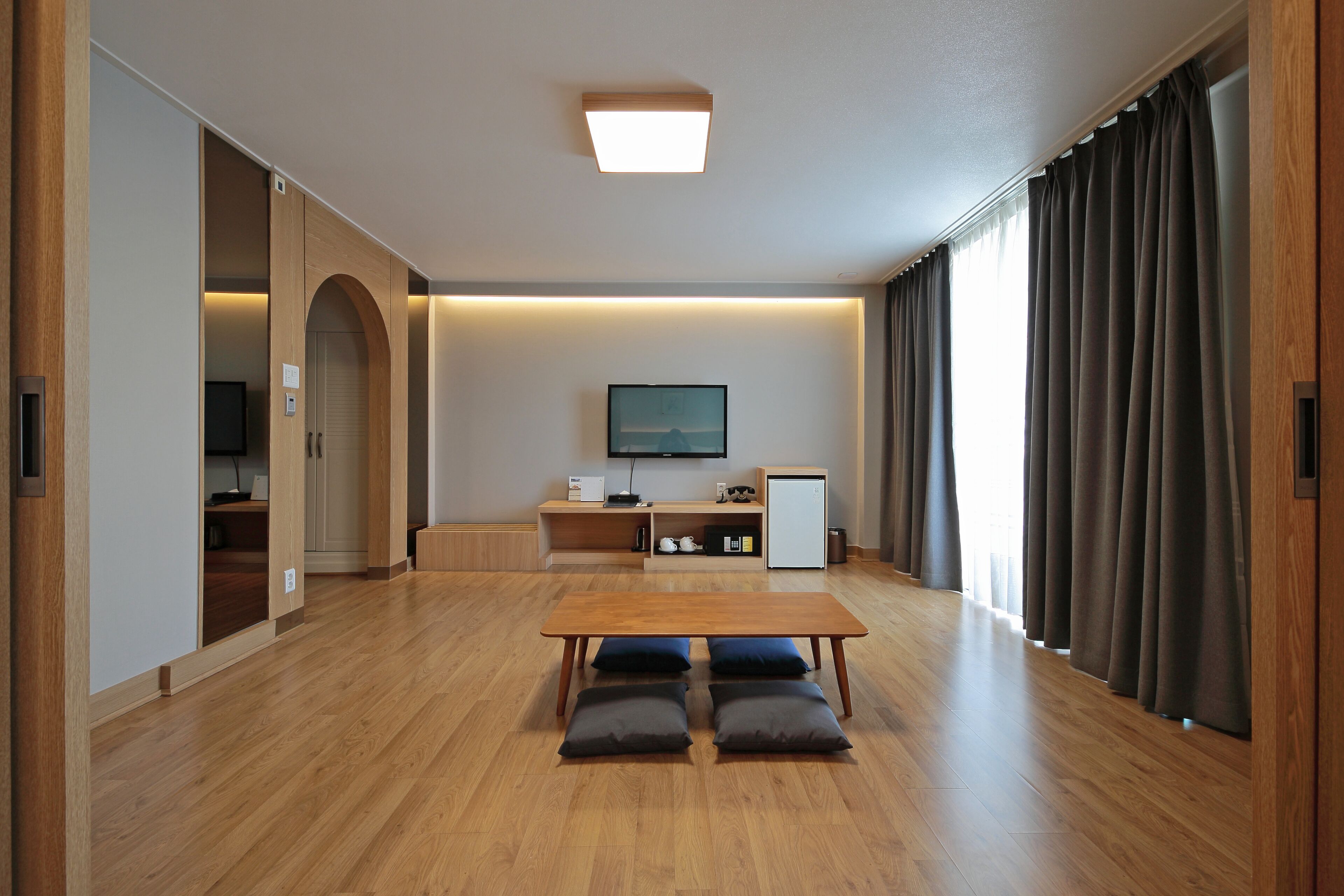Un salón amplio con piso de madera, una mesa central con cojines, una televisión y un mueble empotrado.
