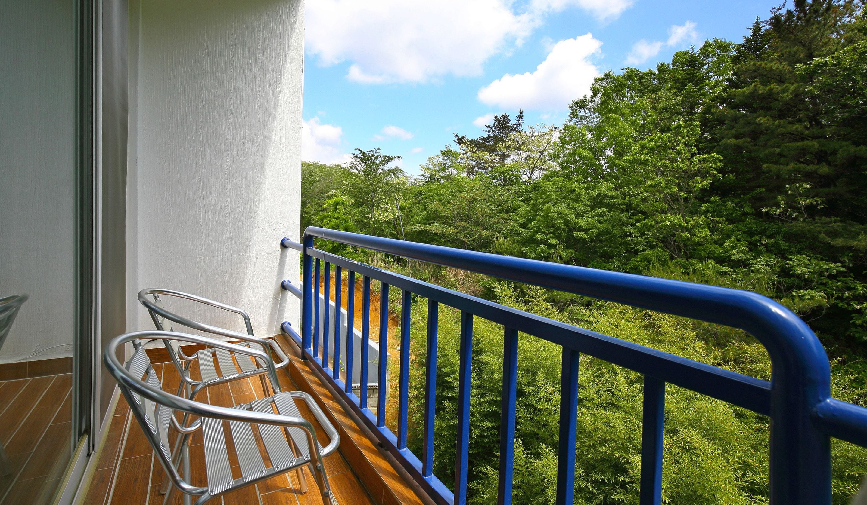 A balcony with a blue railing, a wooden floor, and metal chairs.