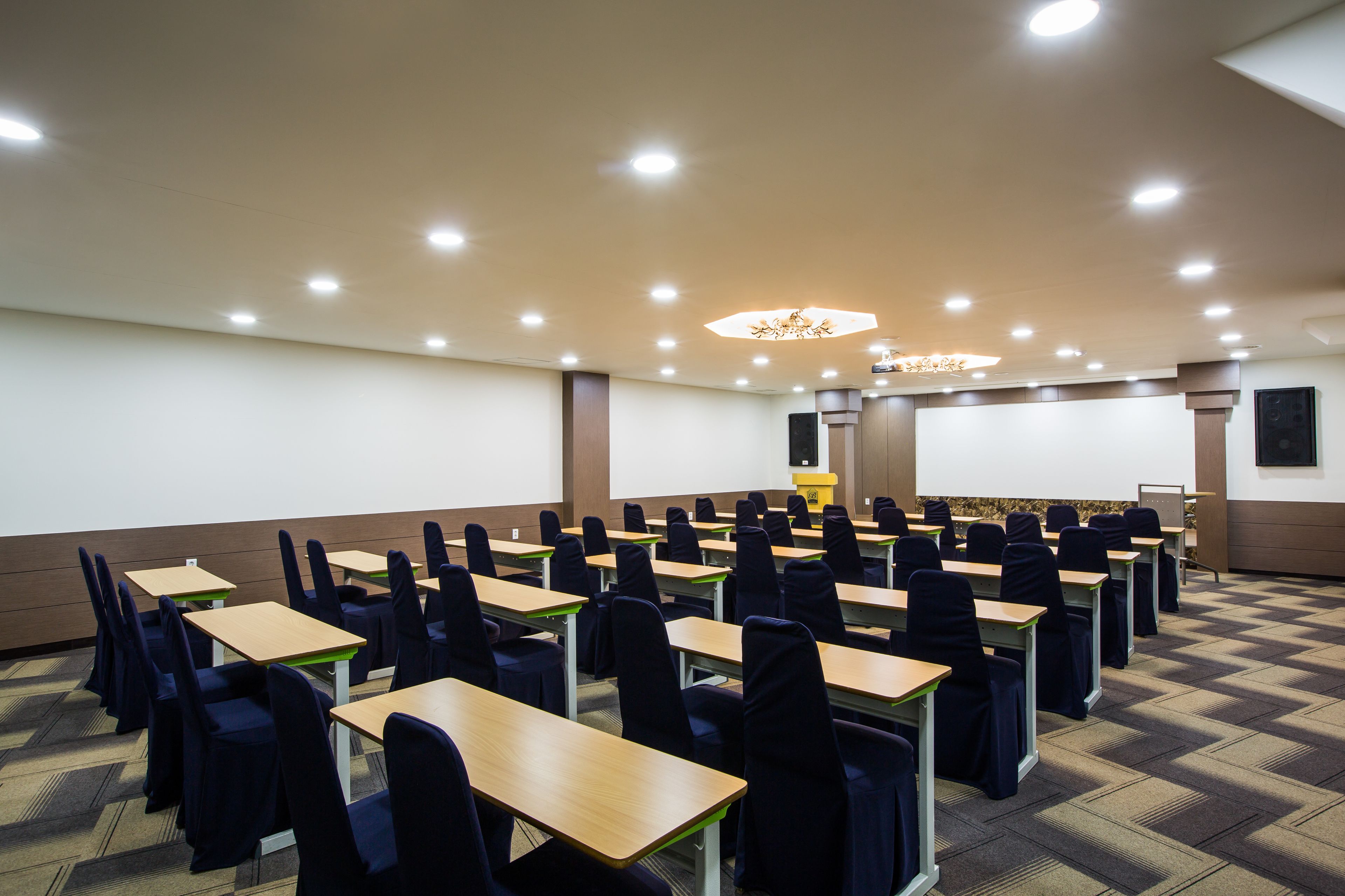 A conference room with rows of tables and chairs, a projector screen, and a podium.