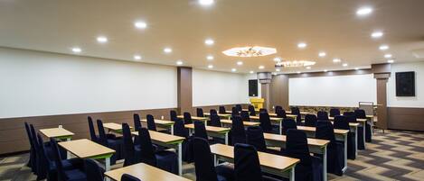 A conference room with rows of tables and chairs, a projector screen, and a podium.