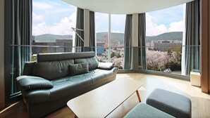 Un salon moderne avec un canapé en cuir, une table basse en bois et une vue sur des cerisiers en fleurs et des montagnes russes au loin.