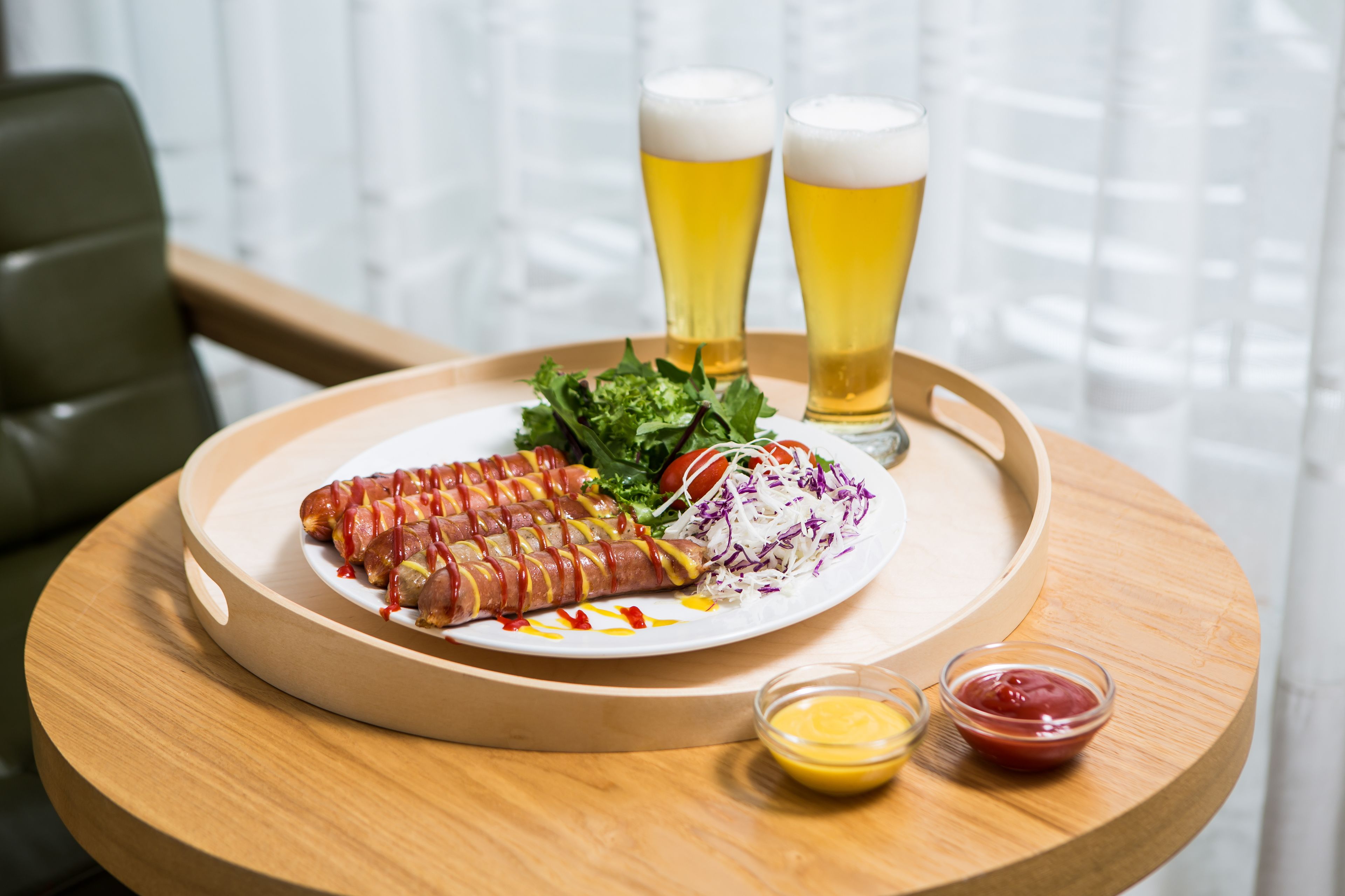 A tray with a plate of food, two glasses of beer, and condiments.