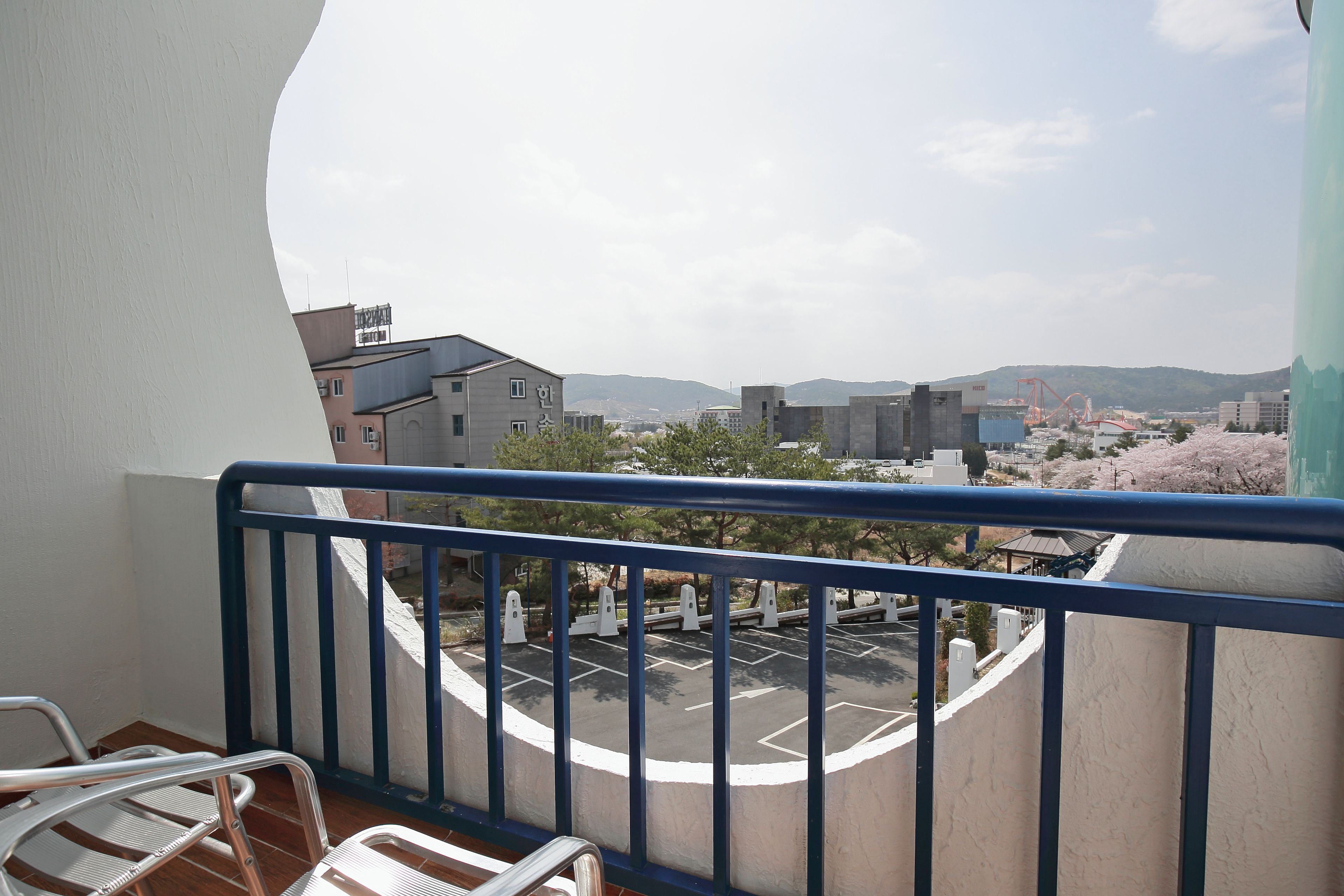 A balcony with a view of a parking lot, buildings, and mountains in the distance.
