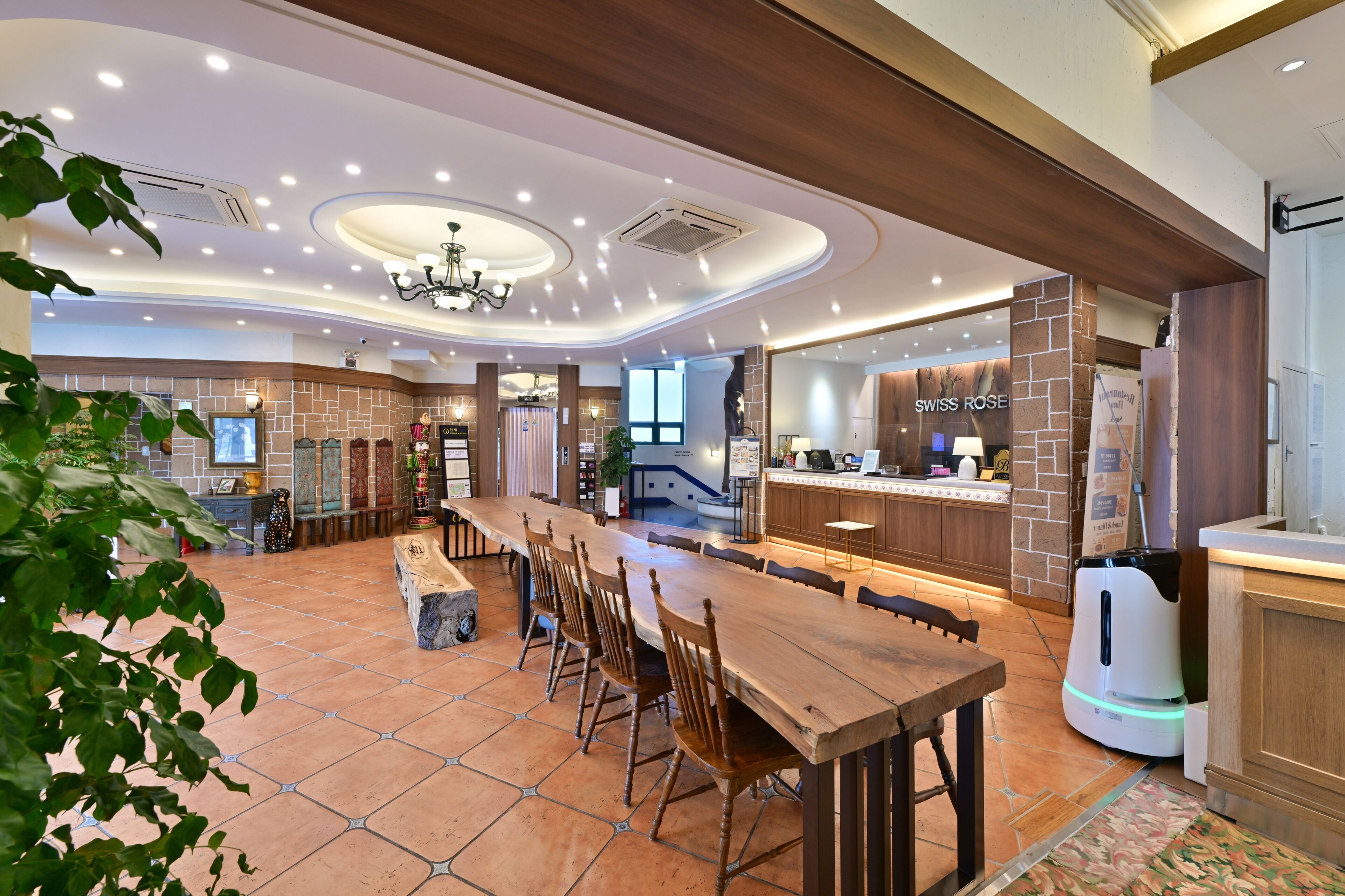 A spacious dining area with a long wooden table and chairs, a bar area with a sign reading 'SWISS ROSE,' and a tiled floor.