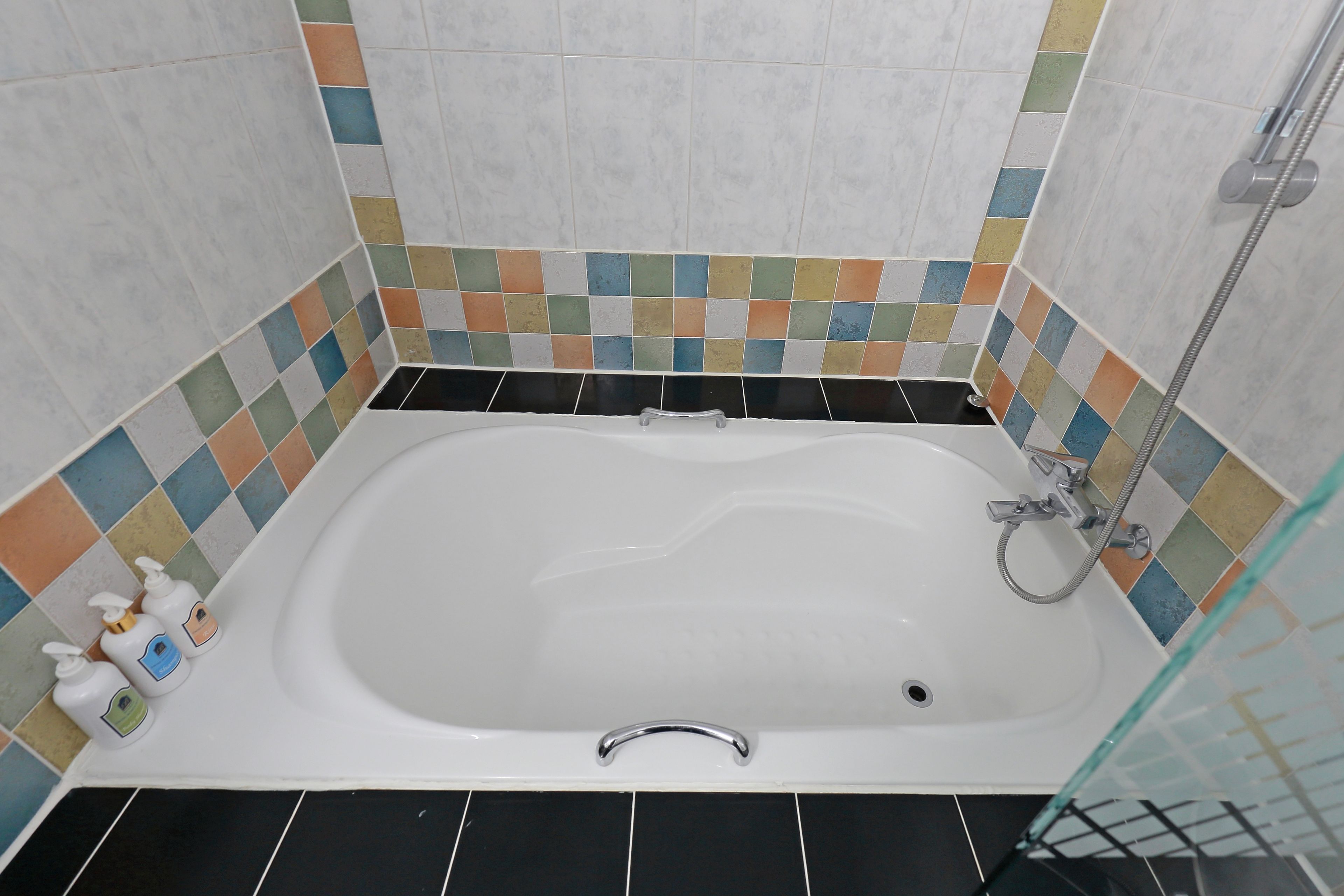 A bathroom with a white bathtub, black floor tiles, and multicolored mosaic tiles on the walls.