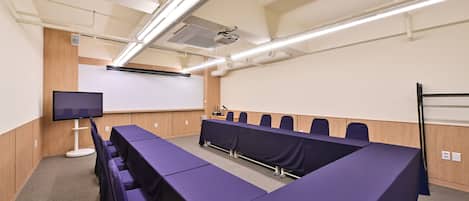 A conference room with a long table, chairs, a projector screen, and a whiteboard.