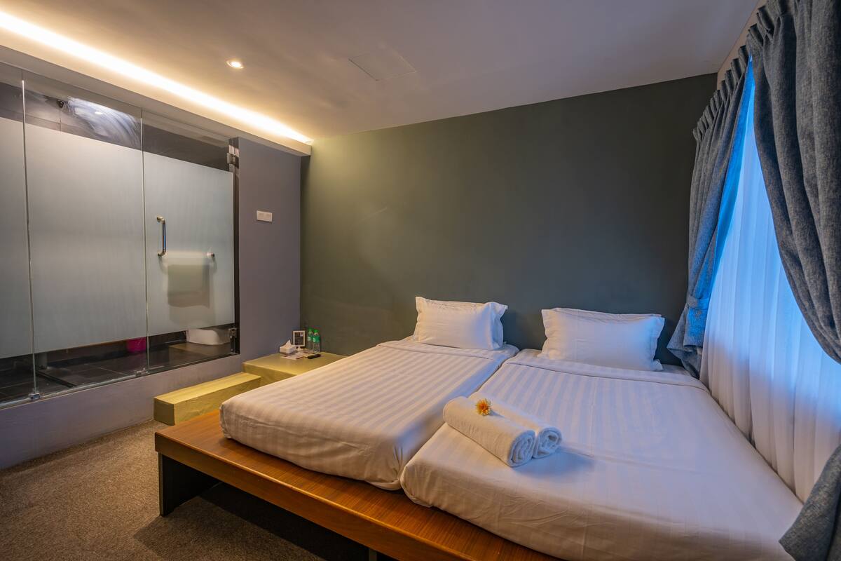 A hotel room with two beds, a wooden bench, a mirror, and a nightstand with toiletries.