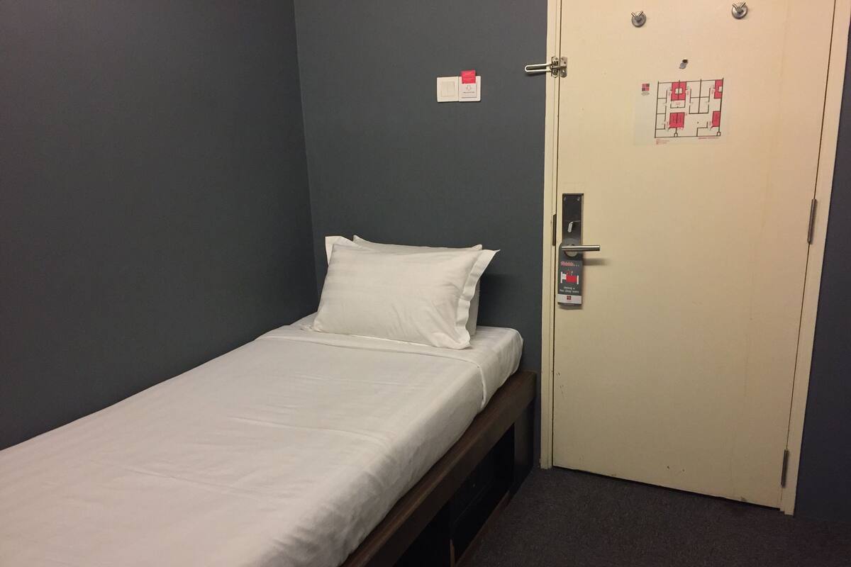 A single bed in a room with a door that has a map and a sign indicating the room number.