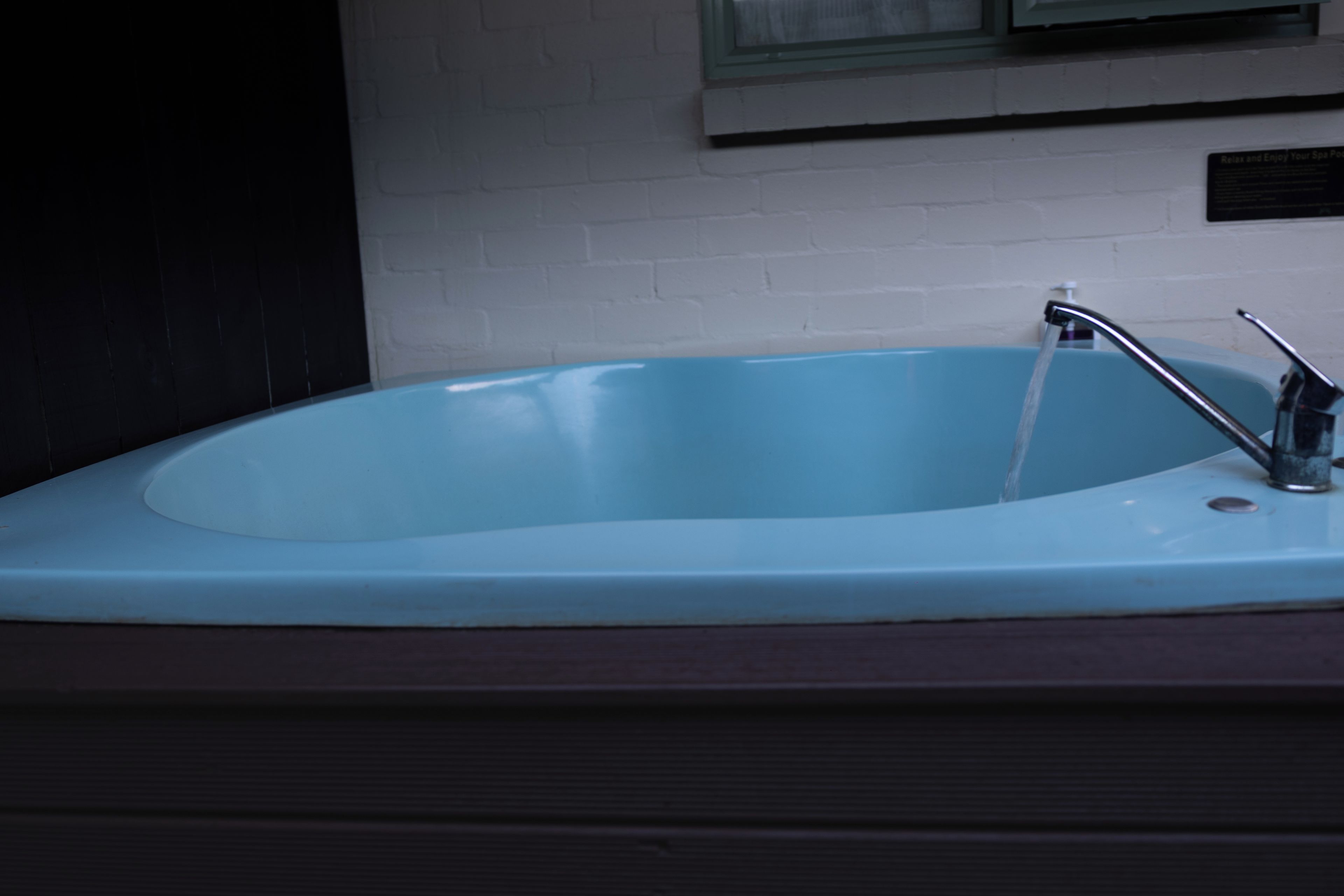 A bathroom with a blue bathtub, a white wall, and a window above the sink.
