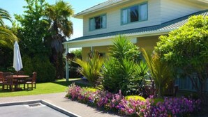 A two-story house with a covered patio, surrounded by lush greenery and flowering plants. - Birchwood Spa Motel (Rotorua)