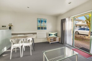 A modern hotel room with a dining area, a TV, artwork on the wall, and a view of the street through the glass door. - Birchwood Spa Motel (Rotorua)