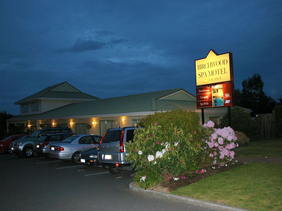A motel with a signboard, parking lot, and a building with a green roof.