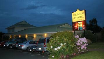 A motel with a signboard, parking lot, and a building with a green roof.