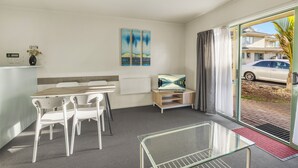 A modern hotel room with a dining area, a TV, artwork on the wall, and a view of the street through the glass door. - Birchwood Spa Motel (Rotorua)