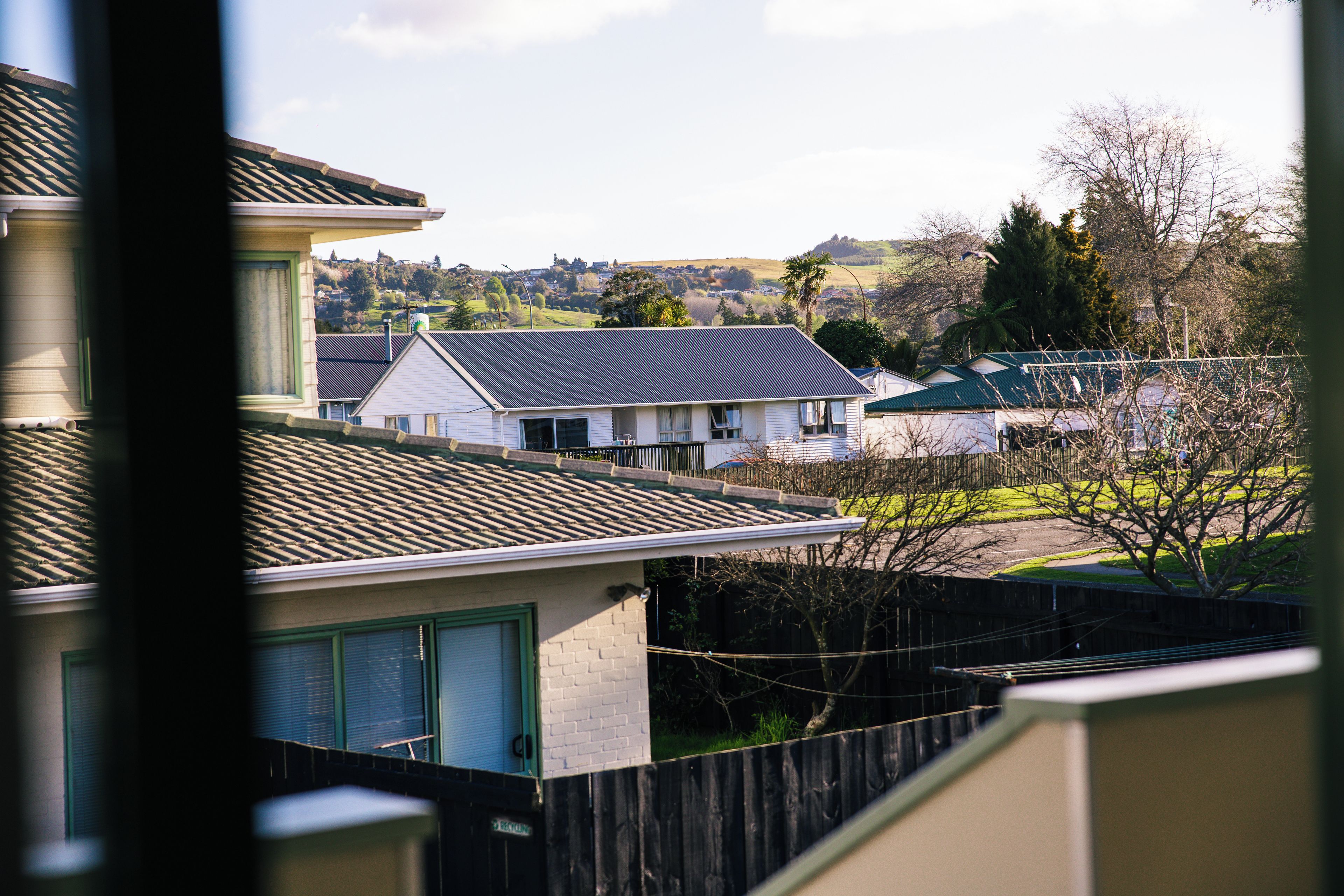 A residential area with houses, a fenced yard, and a hilly landscape in the background.