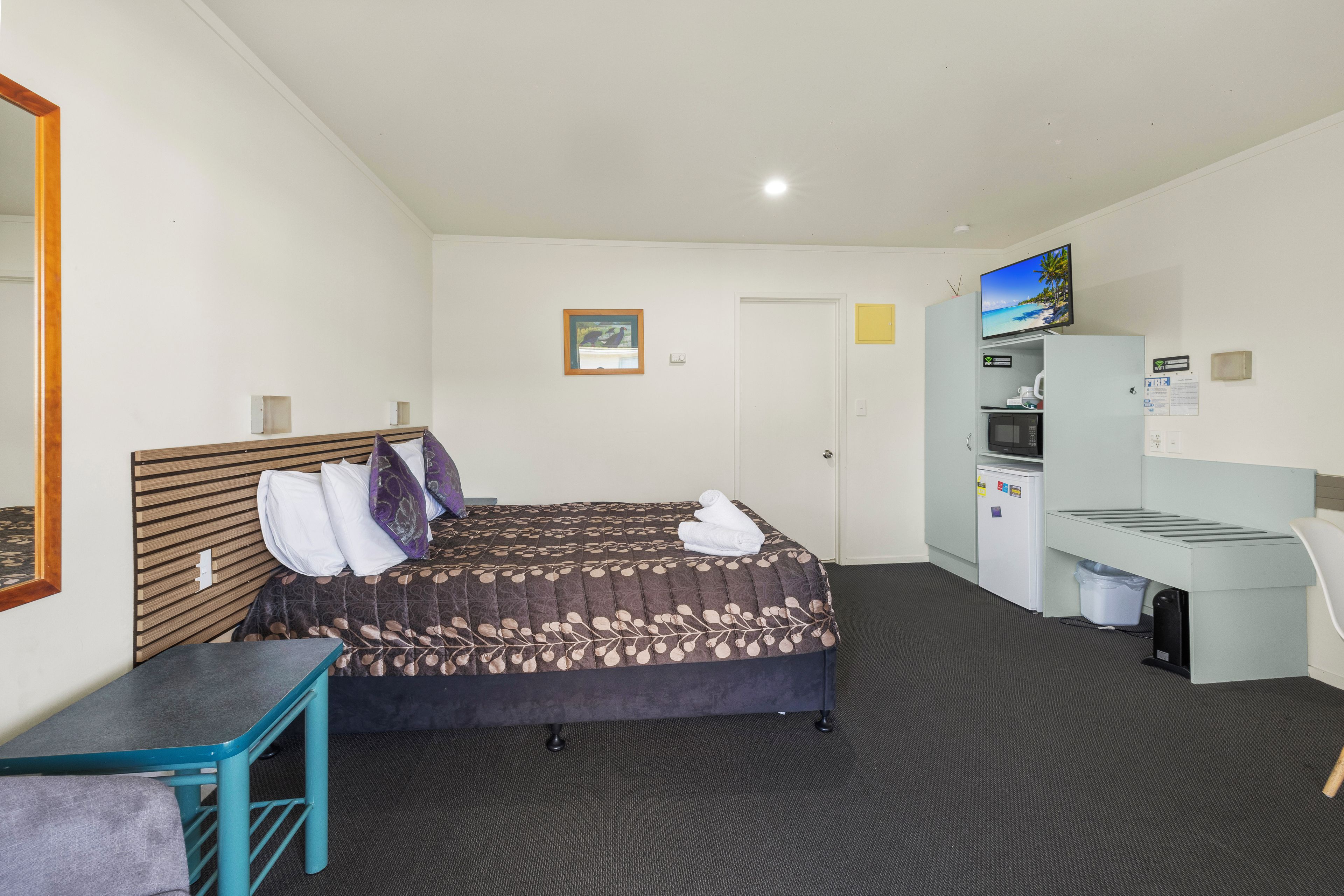 A hotel room with a bed, a desk, a chair, a television, and a microwave.