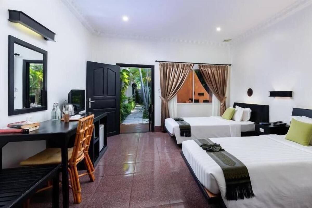 A hotel room with two beds, a desk with a chair, a TV, and a view of greenery outside.