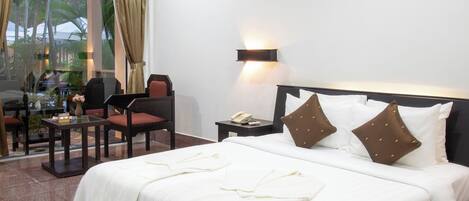 Habitación de hotel con una cama grande, un escritorio con silla, una mesita y vistas a palmeras a través de la ventana.