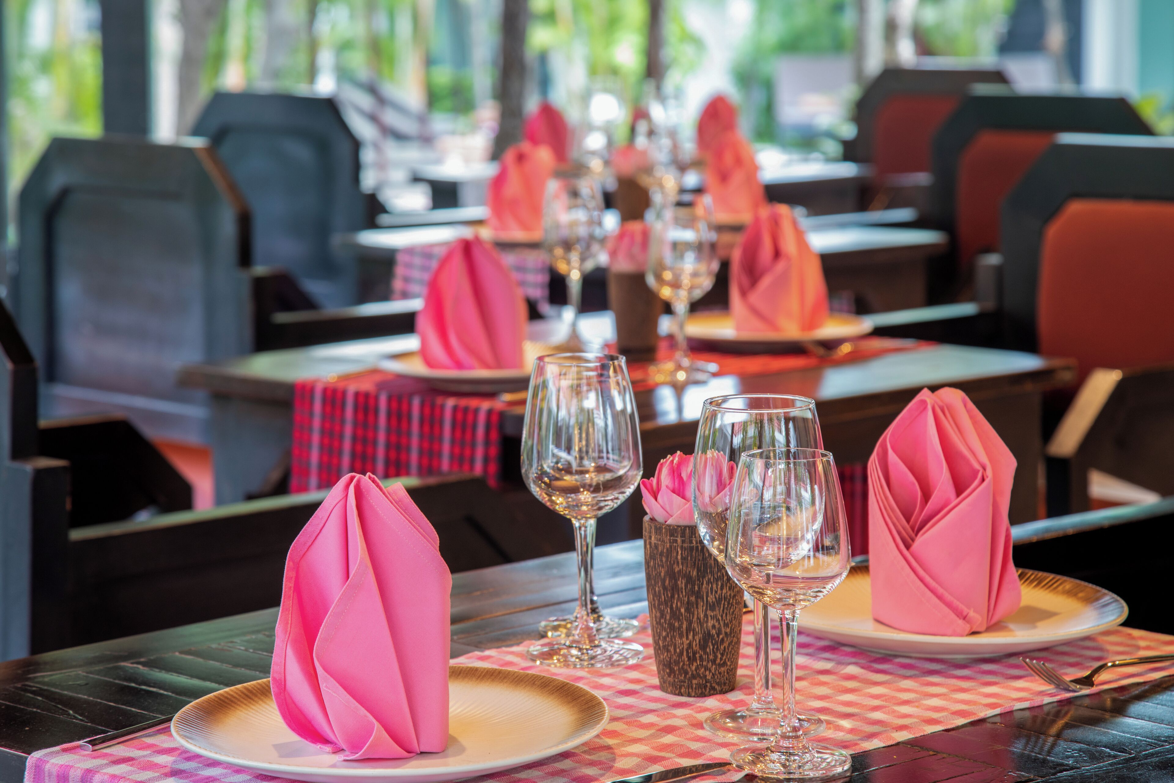 Un ambiente de restaurante con mesas dispuestas para comer, destacando servilletas rosas y copas de vino.
