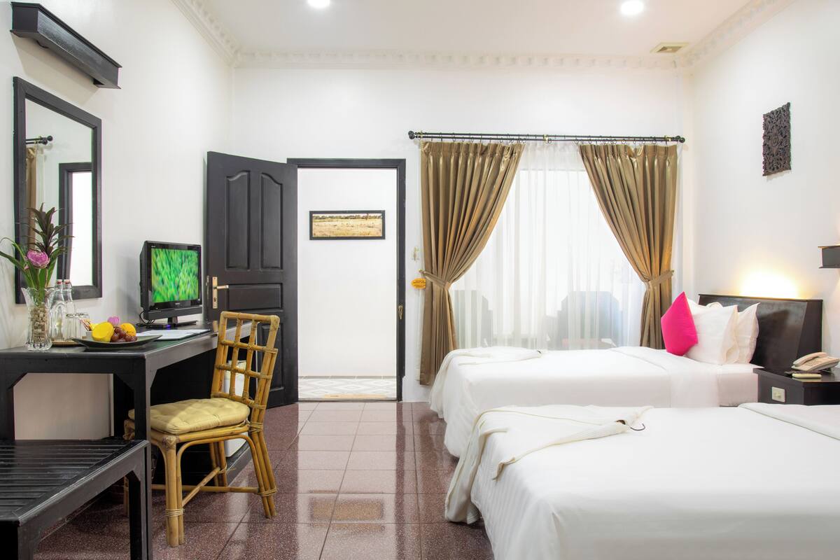 A hotel room with two beds, a desk with a computer, a chair, and a television.