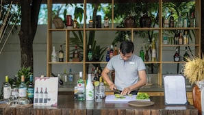 Un espace bar avec un barman préparant des boissons, des étagères remplies de bouteilles d’alcool et un présentoir à menus.