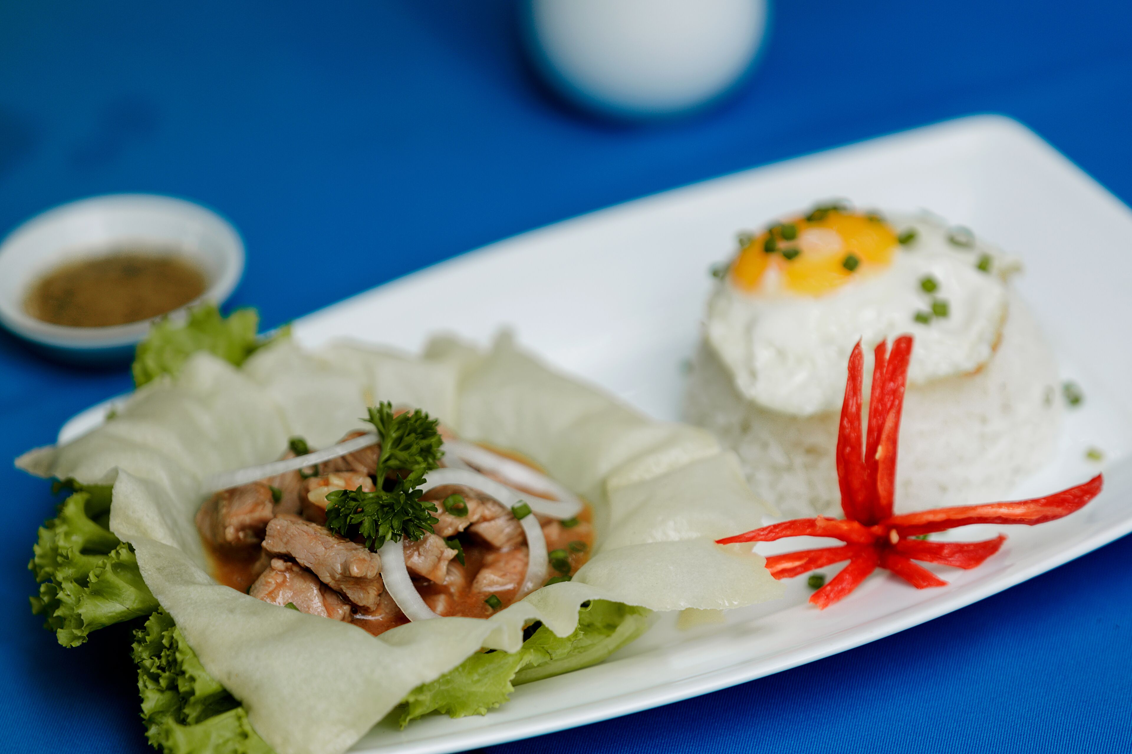 A plate with a wrapped dish containing meat and vegetables, a fried egg, and a small bowl of sauce.