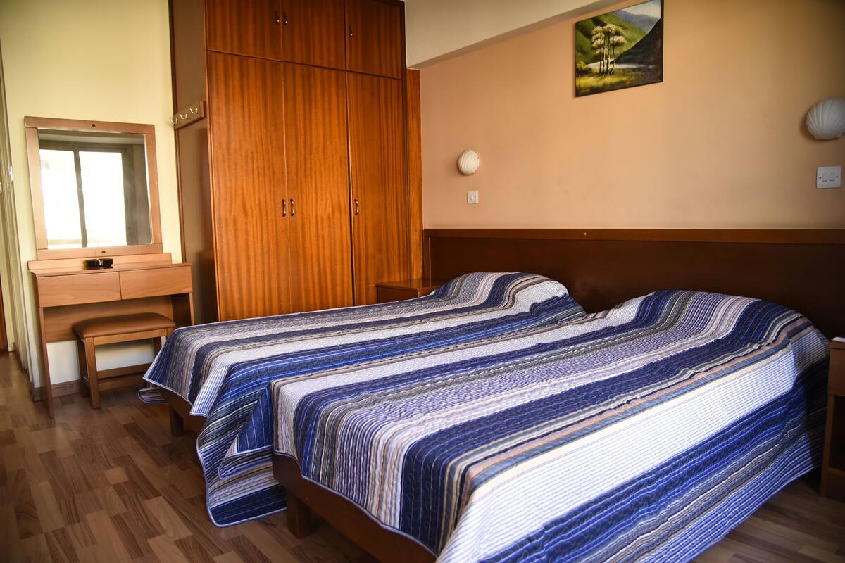 Une chambre avec une armoire en bois, un lit recouvert d’une courtepointe à rayures et un tableau accroché au mur.