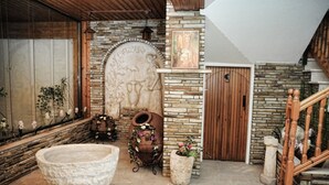 Un interior de paredes de piedra con una gran cuenca de piedra, una escalera de madera y una puerta rústica.