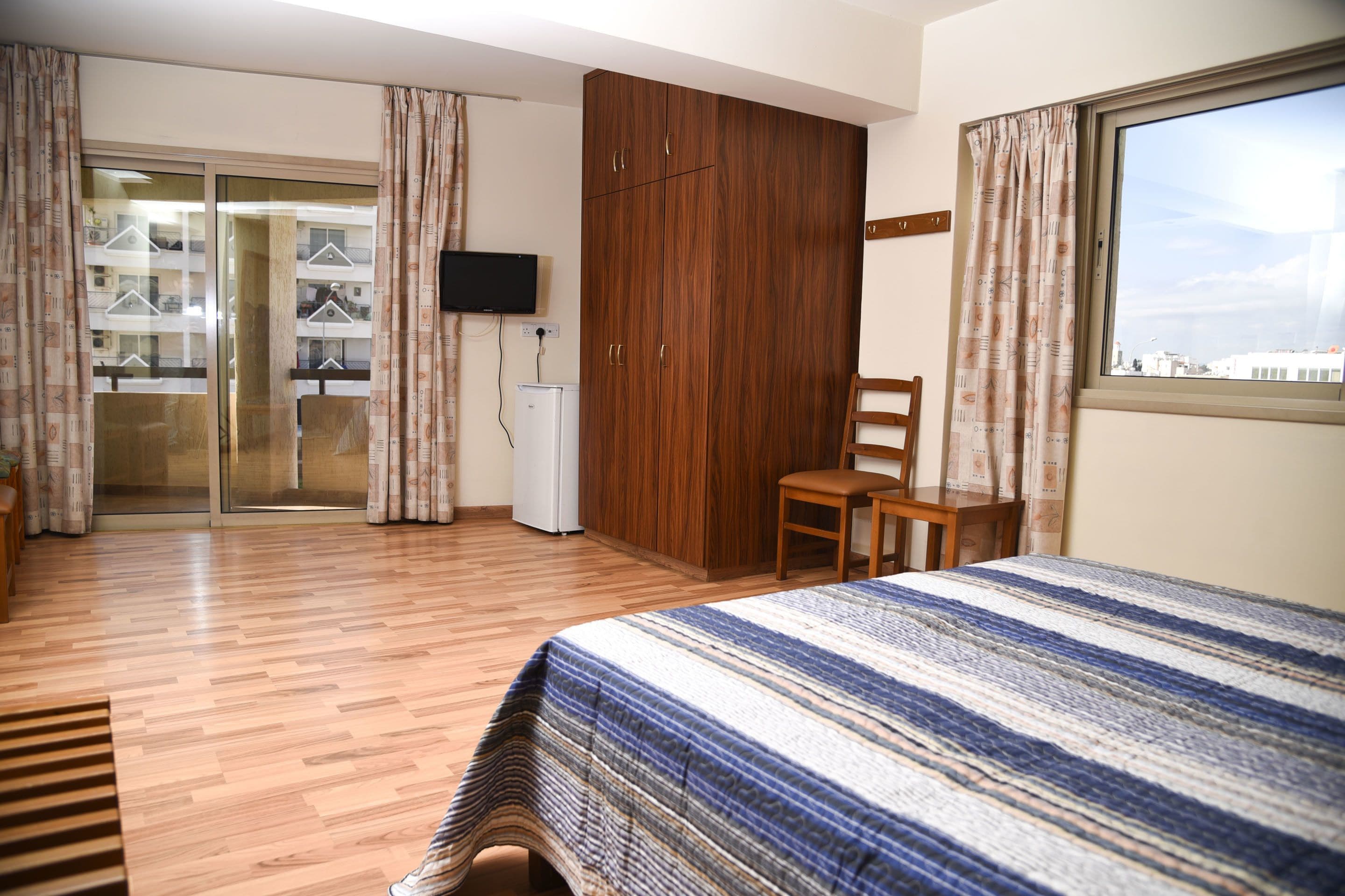 A hotel room with a bed, wooden wardrobe, a desk, and a television.