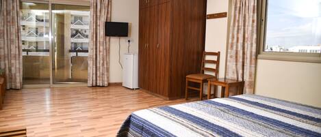 A hotel room with a bed, wooden wardrobe, a desk, and a television.