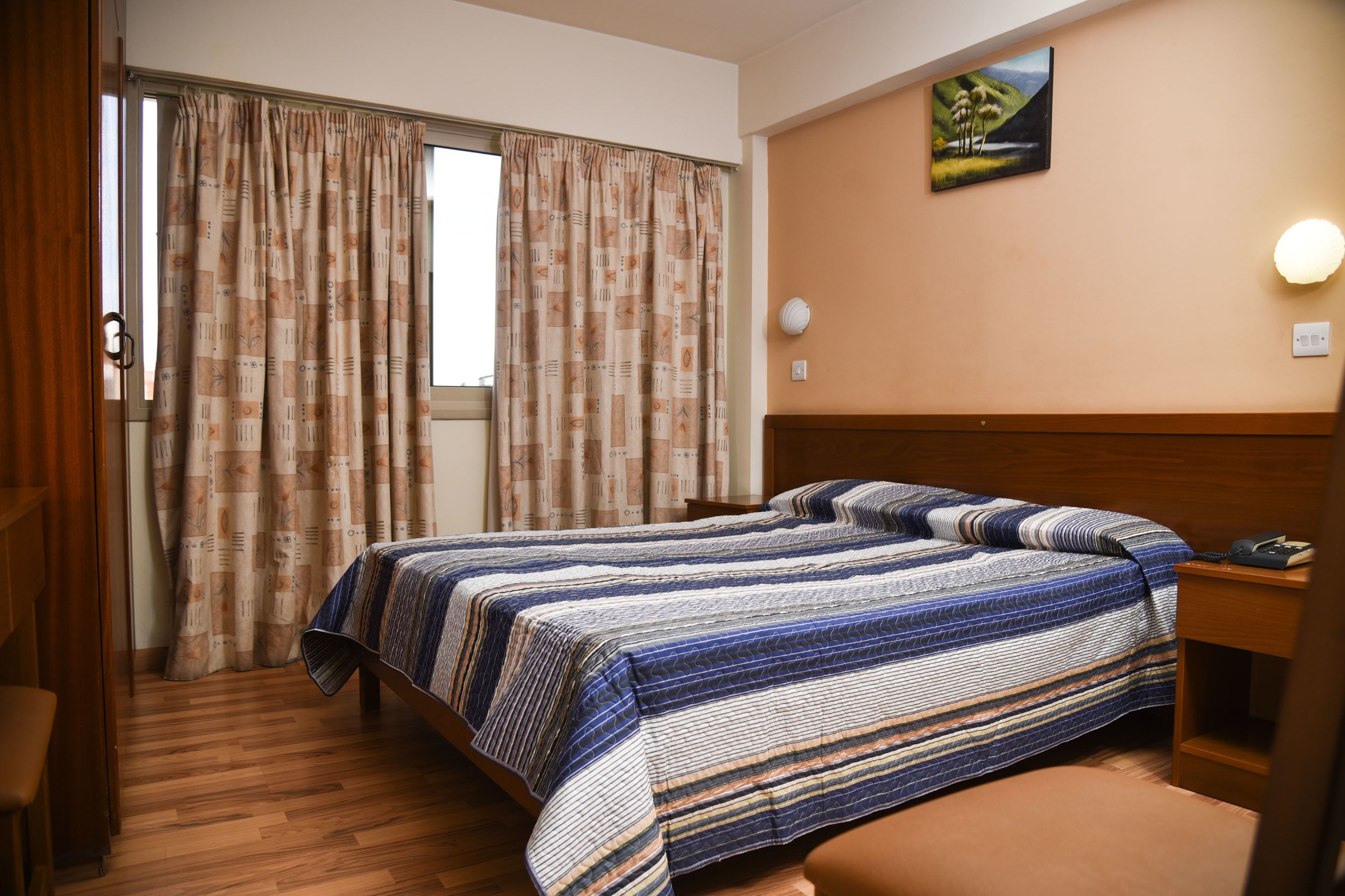 Quarto de hotel com uma cama, mesa de cabeceira, abajur e um quadro na parede.