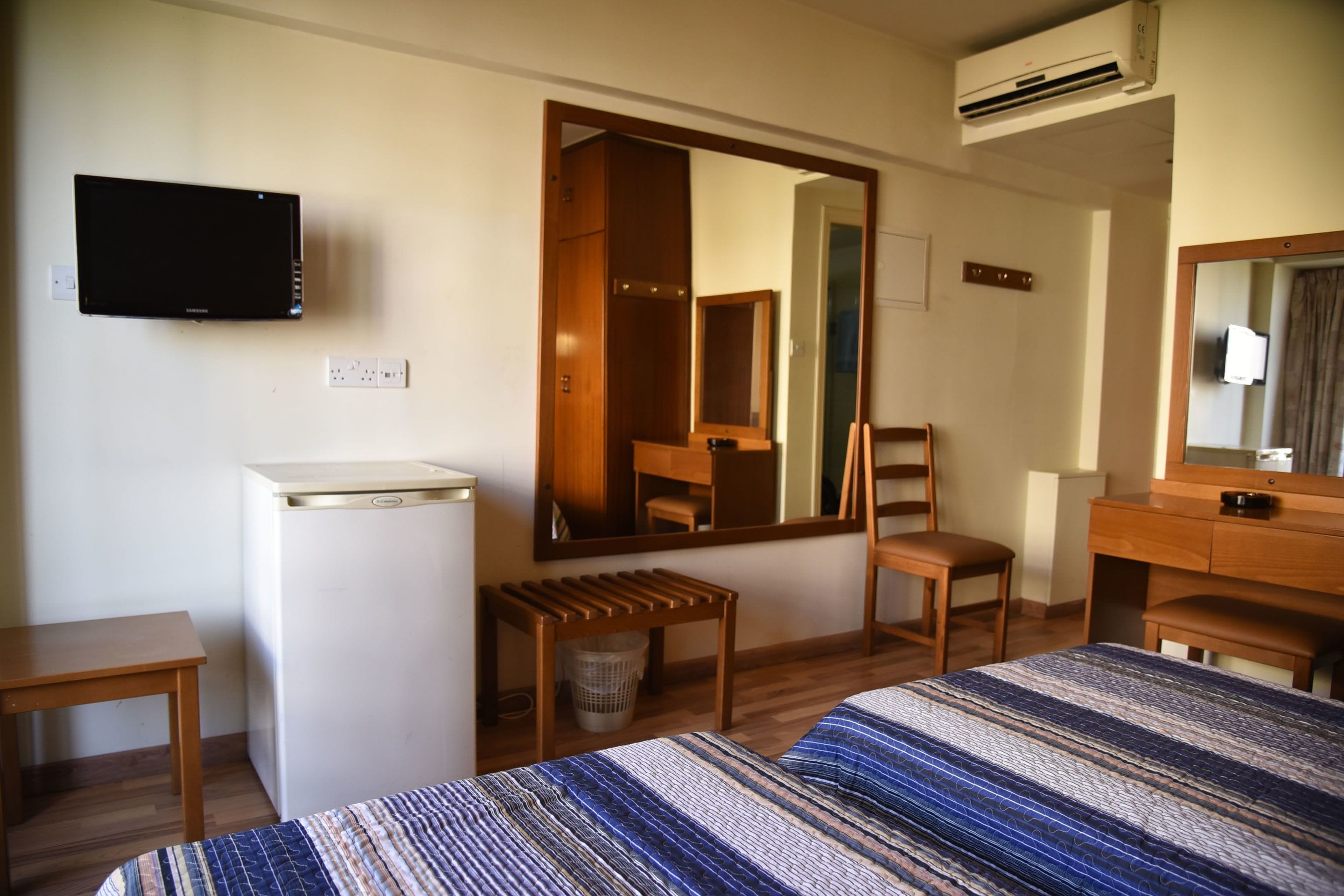 Une chambre d’hôtel équipée d’un lit, d’un bureau, d’une chaise, d’un miroir, d’une télévision et d’un appareil de climatisation.