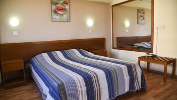 Un dormitorio con una cama de madera, una mesita de noche, un banco, un espejo grande y dos luces fijadas a la pared.