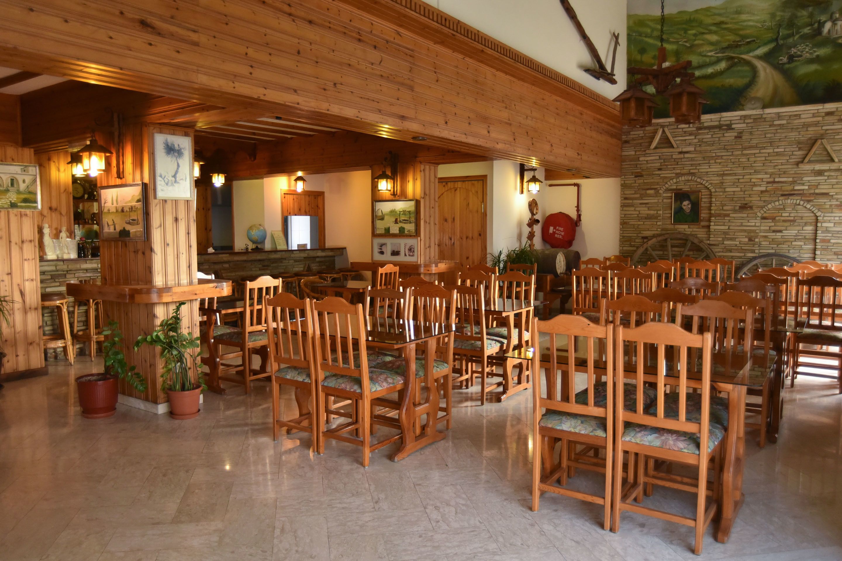 Un restaurante con mesas y sillas de madera, plantas en macetas y un mural en la pared.