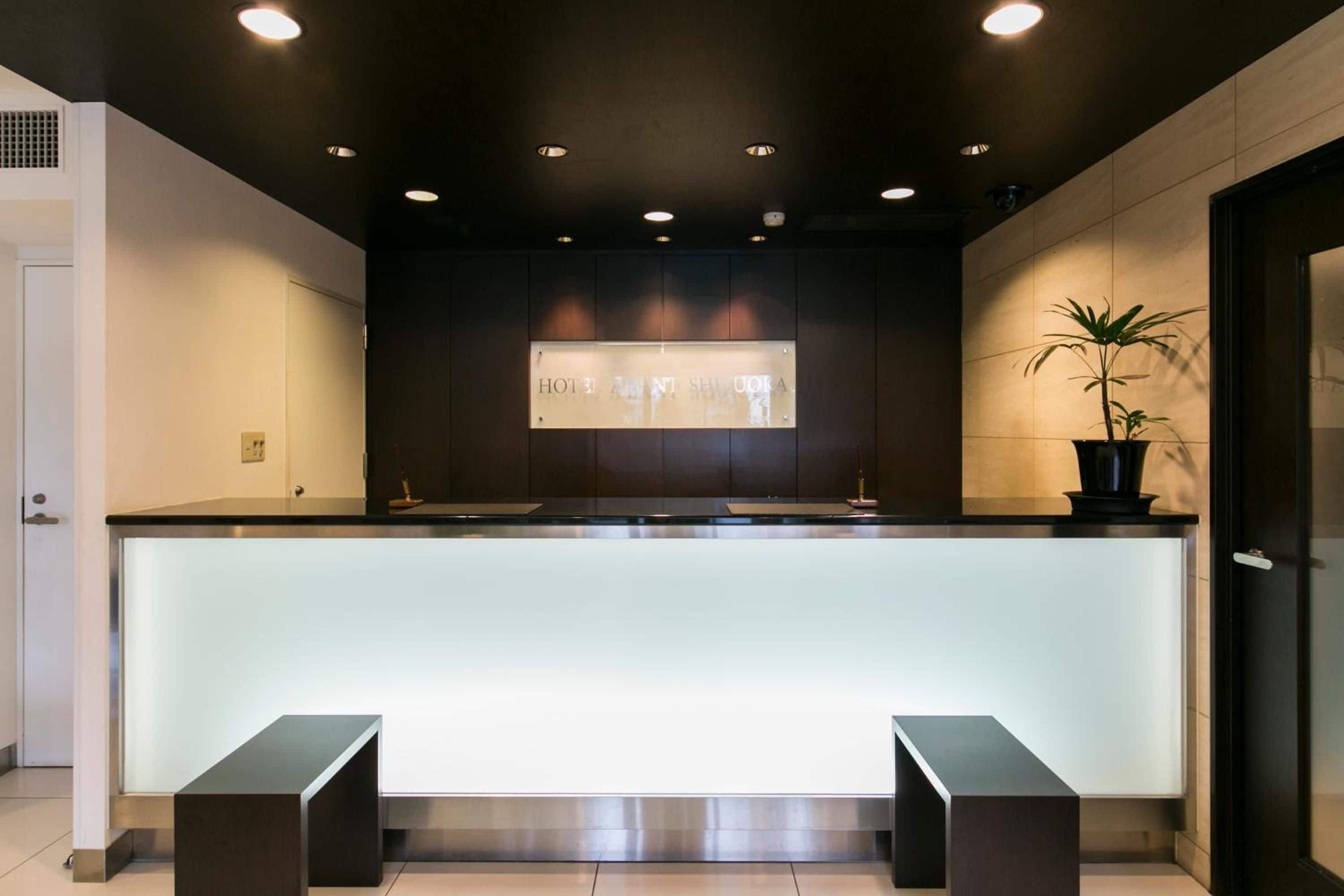 A hotel reception area with a modern design, featuring a reception desk, a potted plant, and a sign above the desk.
