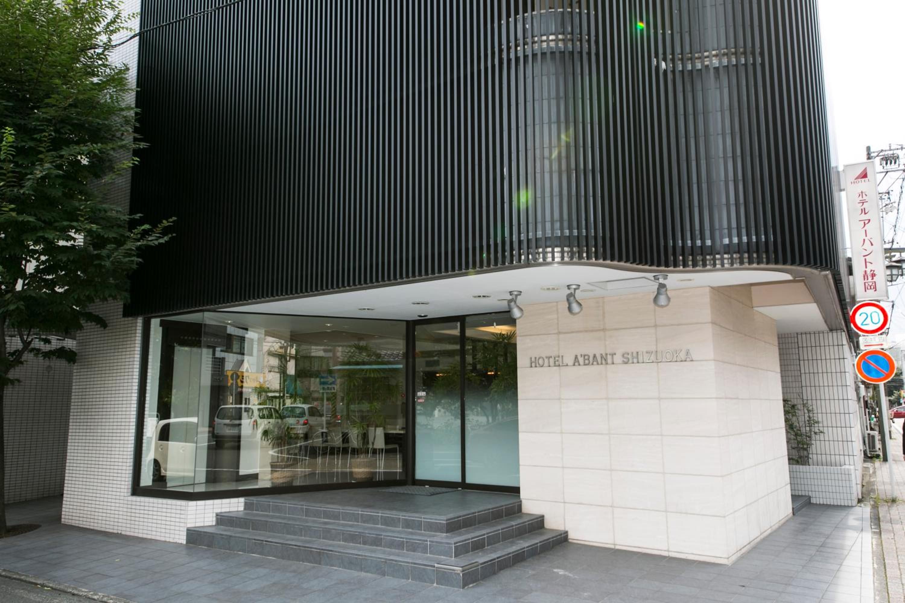 A modern hotel entrance with a glass facade, a set of steps leading up to the entrance, and a sign indicating the hotel name.