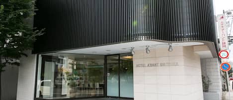Una entrada de hotel moderna con fachada de vidrio, varios escalones que conducen a la entrada, y un letrero que indica el nombre del hotel.