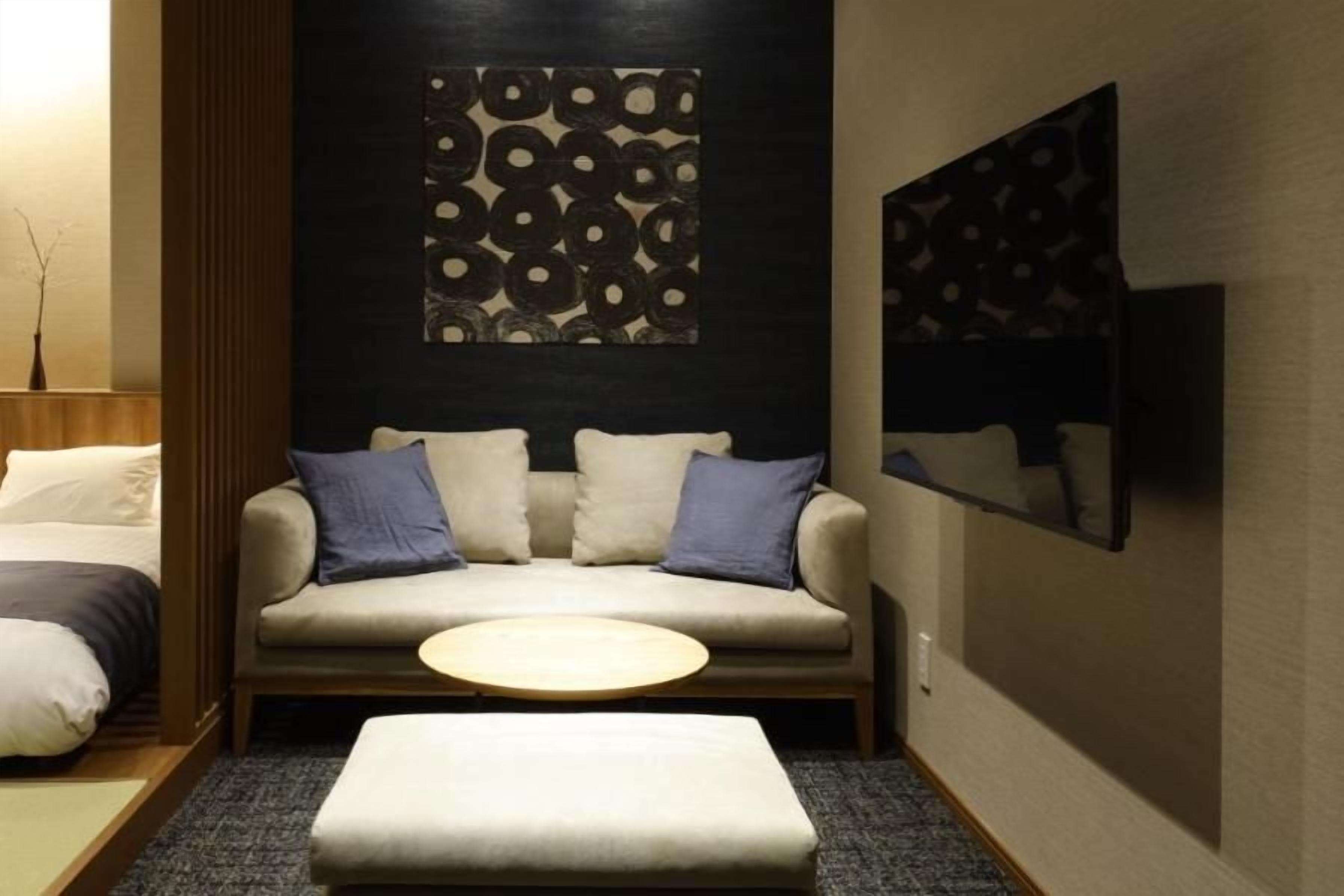 A modern hotel room with a sofa, a round table, and a wall-mounted TV.
